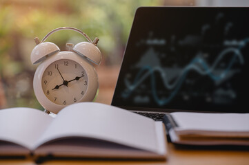 Alarm clock with laptop and notebook on wood desk, calculator and notebook on desk representing...