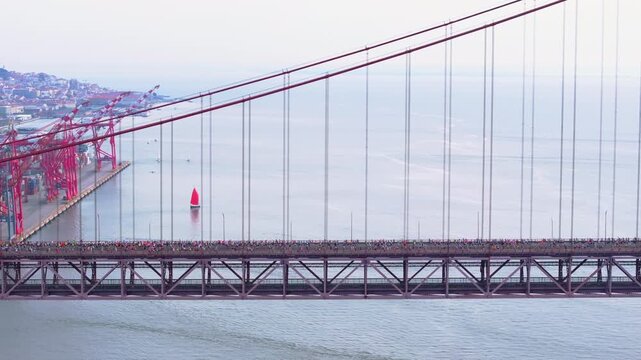 Side-on aerial drone shot of half marathon and 10K long-distance running event in Lisbon, Portugal, Europe. Runners crossing the red 25th April suspension bridge. Commercial grading