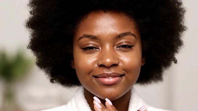 Young Woman Applying Moisturizer - Close-up shot of a beautiful young African-American woman with radiant skin, eyes closed, gently touching her face.