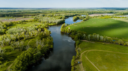 The Ural River, surrounded by green fields in spring, as seen from a drone