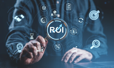 Fototapeta premium Business ROI analysis concept with businessman using magnifying glass to examine return on investment symbol on digital interface background.