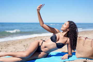 A young woman is joyfully taking a fun selfie at the beach during a stunning summer day