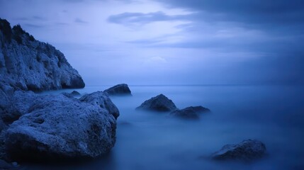 Gentle sea mist rolling in over a rocky shoreline at dusk