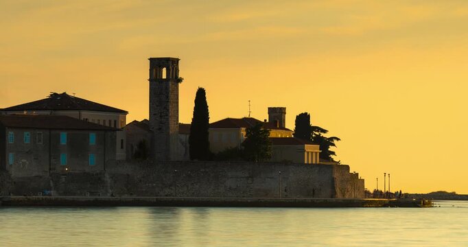 Porec, Croatia - August 13, 2025: Timelapse, zoom out transition. Scenic sunset view of Porec old town skyline with Euphrasian Basilica tower and blurred boat on calm Adriatic Sea in Croatia