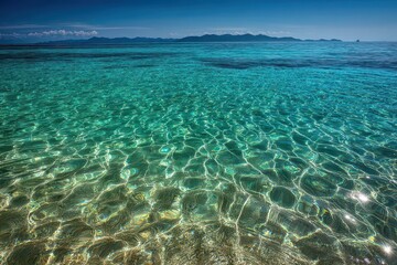 Fototapeta premium Ocean Water with Shimmering Sunlight Reflecting on Surface Turquoise Blue Gradient and Clear Shoreline View of Distant Hilly Island Landscape in Background