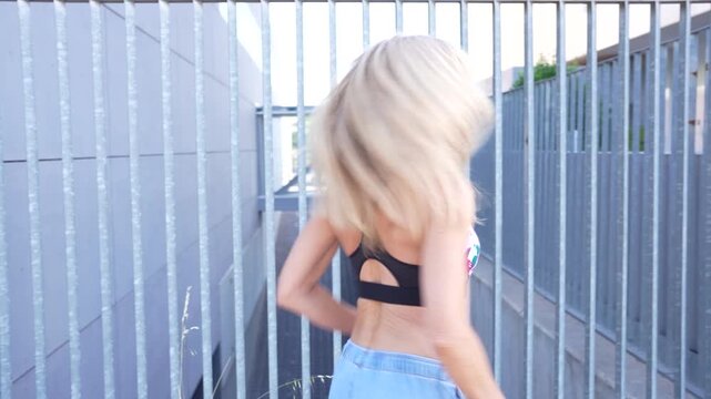 A young woman with blonde hair is walking past a modern building in a colorful top