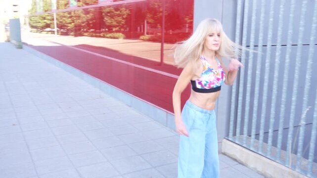A young woman is walking outdoors near a modern building wearing a casual outfit