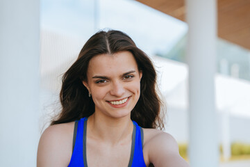 A vibrant portrait of a smiling woman in a blue top with flowing hair, set against an airy backdrop of columns and soft skies.