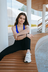 A woman in athletic wear, seated on a curved bench, exudes calm confidence, surrounded by modern architecture and soft lighting.