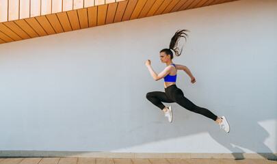 A dynamic jump captured mid-air by a woman in sporty attire, against a minimalist architectural backdrop, embodying energy and athleticism.