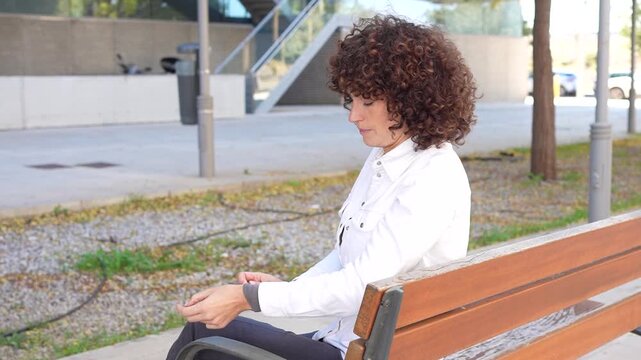 A Thoughtful Young Woman Wearing Stylish Attire Sitting on a Park Bench in Daylight