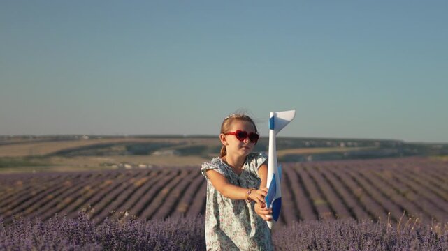 Girl flying toy airplane in beautiful blooming lavender field during sunset