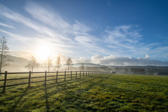 English countryside picture showing a green field at sunrise with a wooden fence acting as a strong leading line. Vibrant blue sky adds to to rural lifestyle and country life feel.