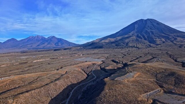 Rising drone shot capturing Mount Misti and the towering Chachani peak bathed in warm golden sunrise light, highlighting the volcanic slopes and rugged Andes landscape under a glorious morning sky.