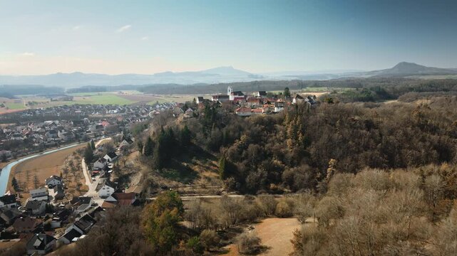Engaging forward drone movement glides toward Aach village on hillside with river curves, autumn trees, fields, and mountain horizons in golden light. Perfect for travel docs, regional ads