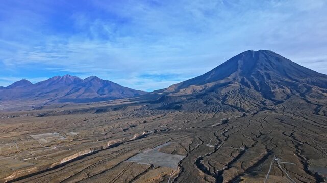 A rising aerial drone shot revealing the towering Mount Misti volcano and the dramatic Chachani mountain peak in the Peruvian Andes under a bright blue sky on a clear sunny day.