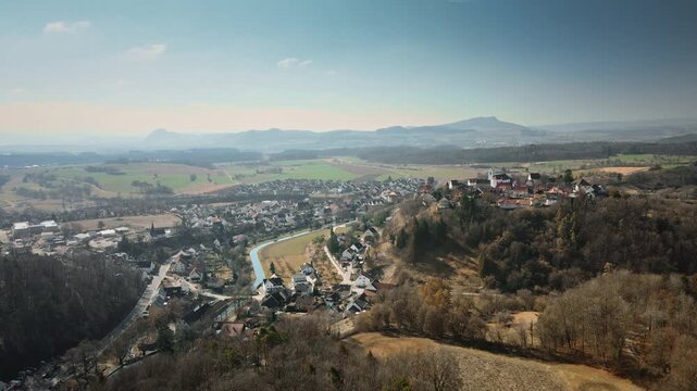 Immersive forward drone flight dives into picturesque Aach village hugging a meandering river, framed by autumnal fields, lush forests, and layered hills in vibrant daylight.