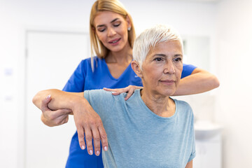 professional female physiotherapist in blue scrubs providing manual guidance to a senior woman...