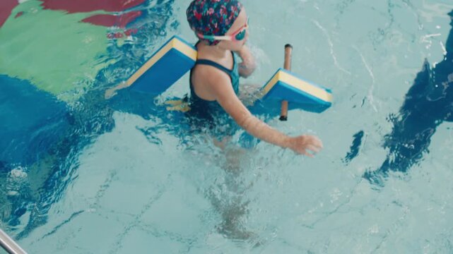 Kid learns swimming. Pre teen girl swims in the public swimming pool with water toy