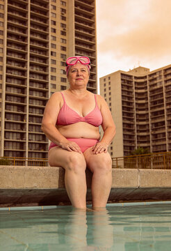 dickere Frau auf sitzt auf einer Poolmauer mit rosa bikini und Schwimmbrille