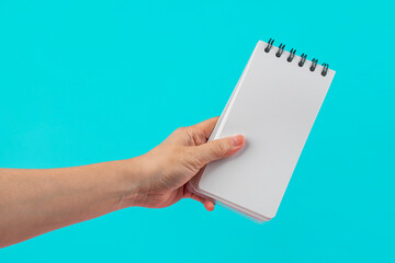 A white notebook in hand against a blue background.