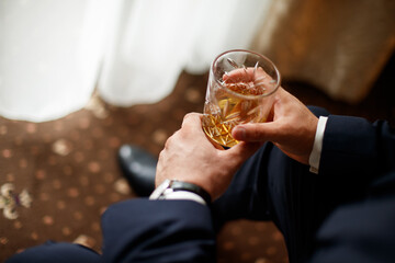A man is holding a glass of alcohol. The man is wearing a white shirt and black pants