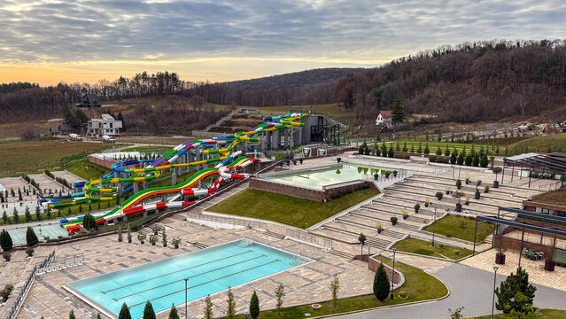 Colorful serpentine waterslides weave through tranquil rural aquapark landscape, evoking Eclectica Festival and World Water Day celebration