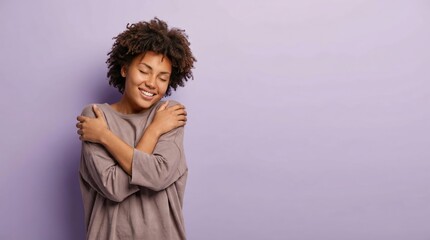 Young african american woman with curly hair embracing herself and smiling brightly with closed eyes against a purple studio backdrop and copy space