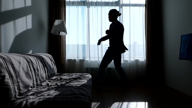 Young business man feel high and successful and do frolic dance against window, silhouetted slow motion shot. Hipster guy in formal suit move body and throw hands out, celebrate some achievement