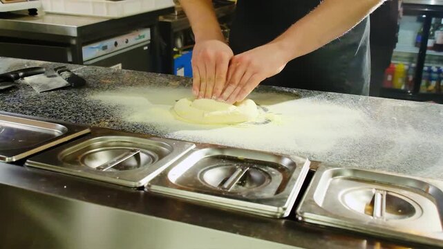 Focused pizza chef presses pizza dough with knuckles feeling elasticity change under fingers. Man works dough into flexible uniform mass. Slow motion