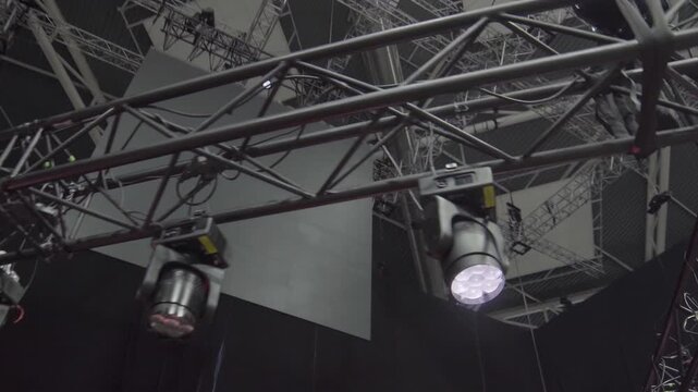Moving spotlights emit sharp beams illuminating hanging LED panel. Lighting flickers rhythmically revealing concert system synchronization