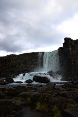 Fototapeta premium Waterfall flowing through the tectonic rift of UNESCO Thingvellir National Park, Iceland. Volcanic rocks and dramatic water movement symbolize natural forces, geological time and resilience.