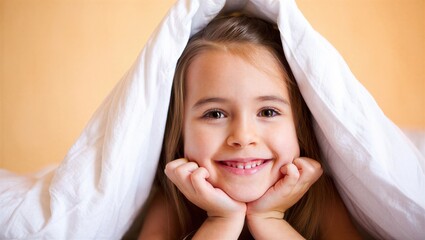 A young girl with long hair smiles while resting under a white blanket in a warm, cozy bedroom. Joyful childhood moment.