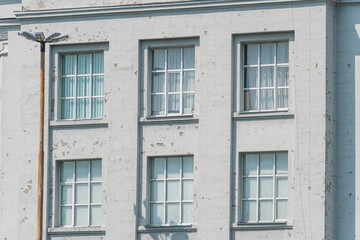 Obraz premium A street-level image of a public building facade with uniformly spaced, metal-framed windows The building shows signs of wear and is primarily colored in shades of the base material, darker on windo