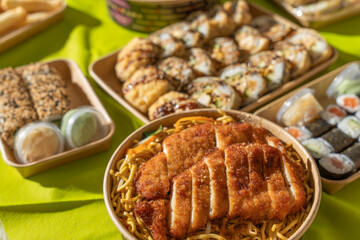 Asian takeaway meal with fried sushi rolls, spring rolls, and breaded chicken noodles on a green...