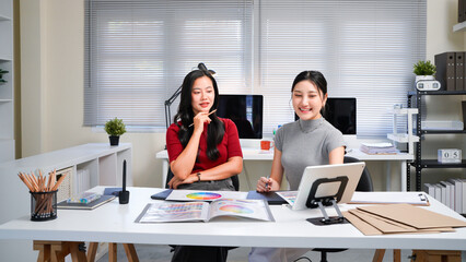Two professional women collaborating on creative design project, discussing colorful color swatches, hues, and palettes at modern office workspace table. Ideal for wallpaper, poster