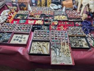 A collection of traditional Indonesian antiques and accessories featuring various gemstone rings, ancient coins, small keris, and amulets arranged on a table.