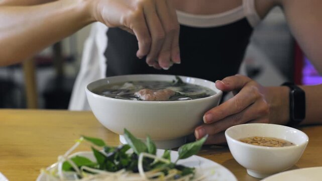 Preparing and seasoning traditional pho soup with fresh herbs and spices