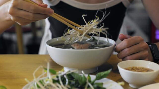 Person enjoys vietnamese pho with chopsticks in a cozy restaurant setting