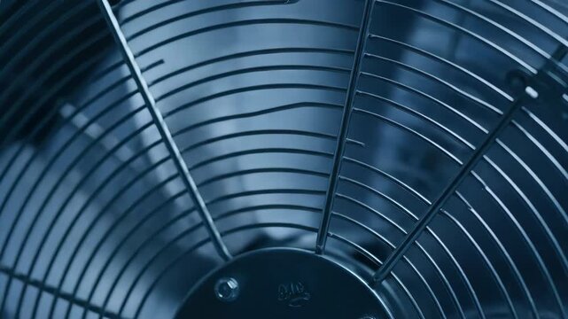 Close-up of a dark blue industrial fan grill with blurred rotating blades.