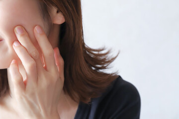 頬を指で押さえる女性のクローズアップ　肌トラブルと敏感肌のイメージ