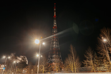 Communication tower illuminated at night with surrounding streetlights and trees, showcasing urban...