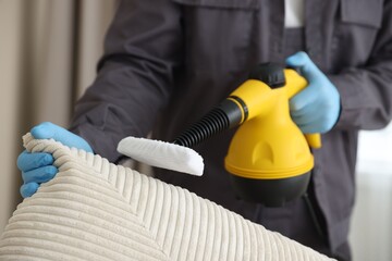 Pest control worker cleaning sofa with steam cleaner indoors, closeup