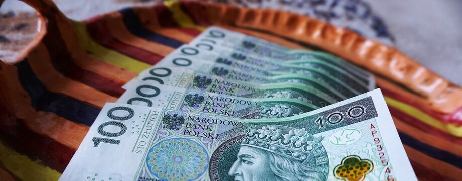 Kilka banknot&oacute;w 100 zł leży na kolorowej tacy, wyeksponowane w porządku. 