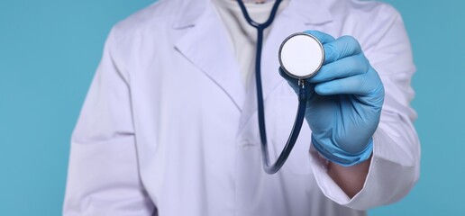 Doctor with stethoscope on light blue background, selective focus