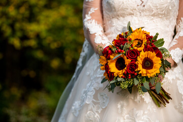 A bride dressed in an elegant long-sleeved wedding gown holds a stunning bouquet of golden...