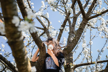 low angle view of girl holding flowers in front of her face standing against blooming tree