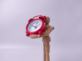 Small, red, retro-style analog alarm clock held by a wooden articulated mannequin