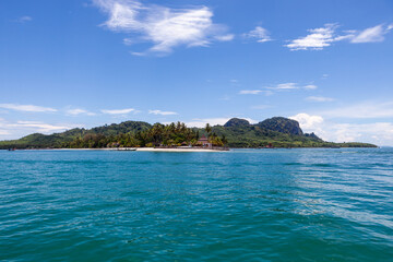 Naklejka premium Tropical island of Koh Muk in Thailand with lush greenery and clear blue sea. Sandy beach along the coastline with palm trees. Calm ocean waters under a bright sky. Remote Andaman Sea location.
