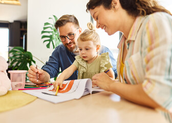 Fototapeta premium Portrait of a little girl and mother and father or teacher coloring a book in classroom or at home. Education and development concepts